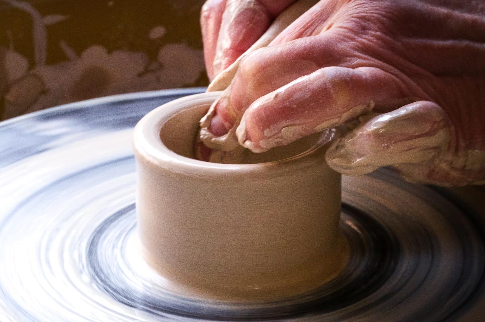 Hands shaping wet clay on a spinning pottery wheel, forming a small ceramic vessel.