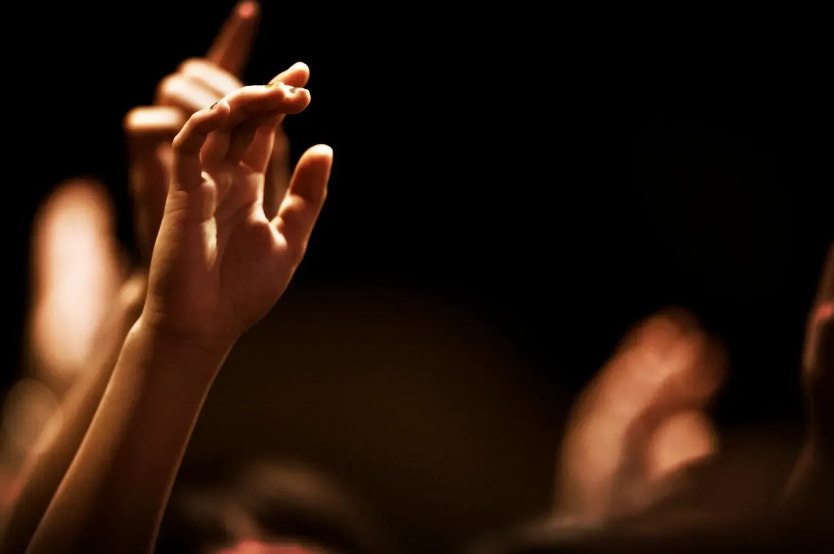 A student’s hand raised in a dark classroom, representing the active engagement in learning and the foundational step of questioning within an apprenticeship.