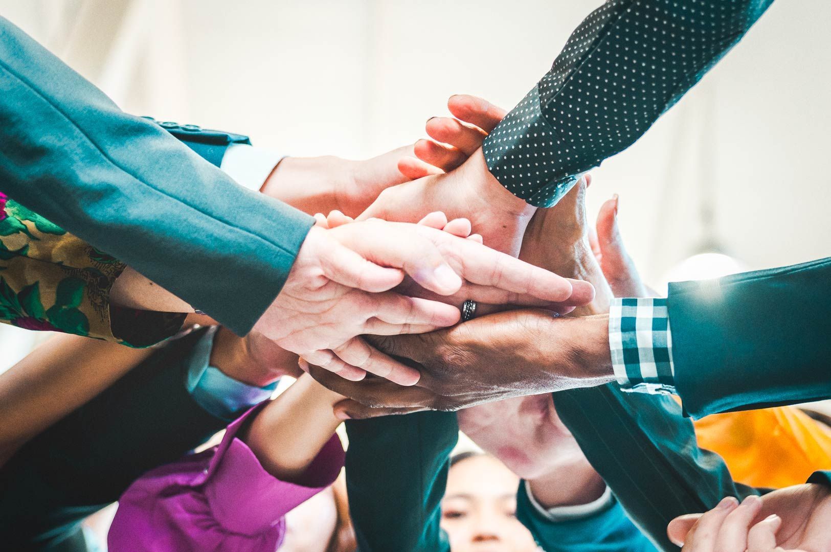 Employees in colorful business attire joining hands in unity, representing collaboration and workplace culture.