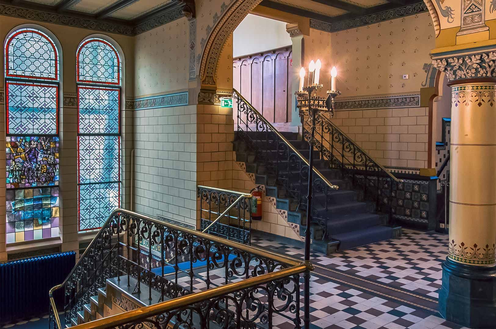 Vintage interior featuring tiled floors, ornate railings, stained glass windows, and a grand staircase.