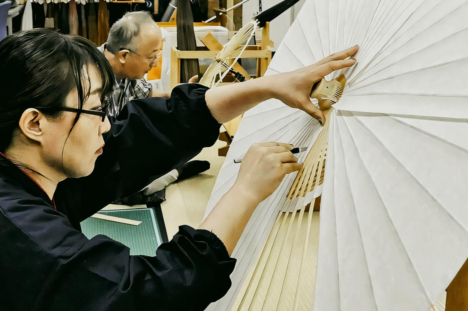 Artisans crafting traditional Japanese paper umbrellas (wagasa) in a workshop, attaching paper to wooden frames.