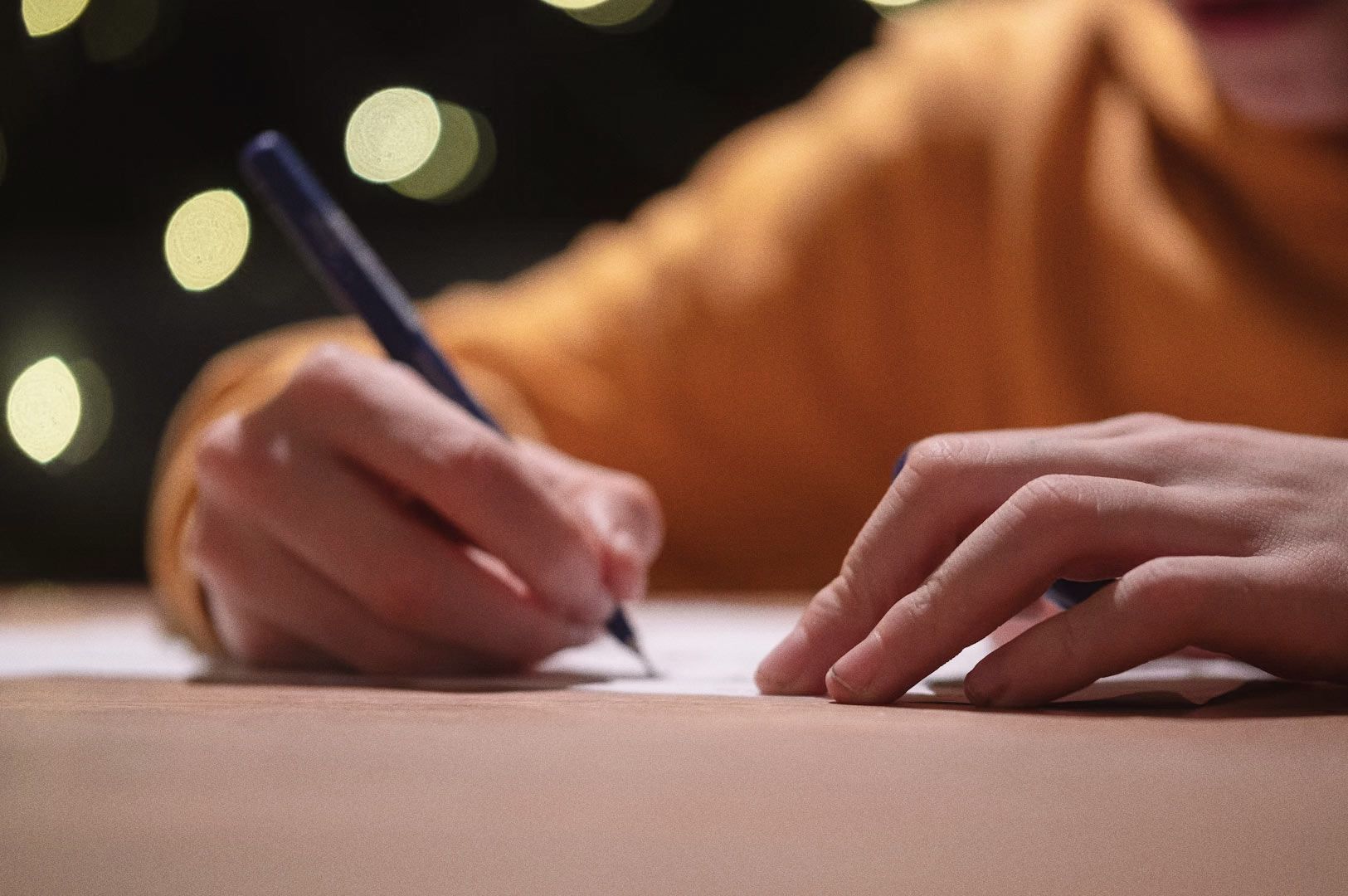 Close-up of hands writing on paper with blurred lights in the background