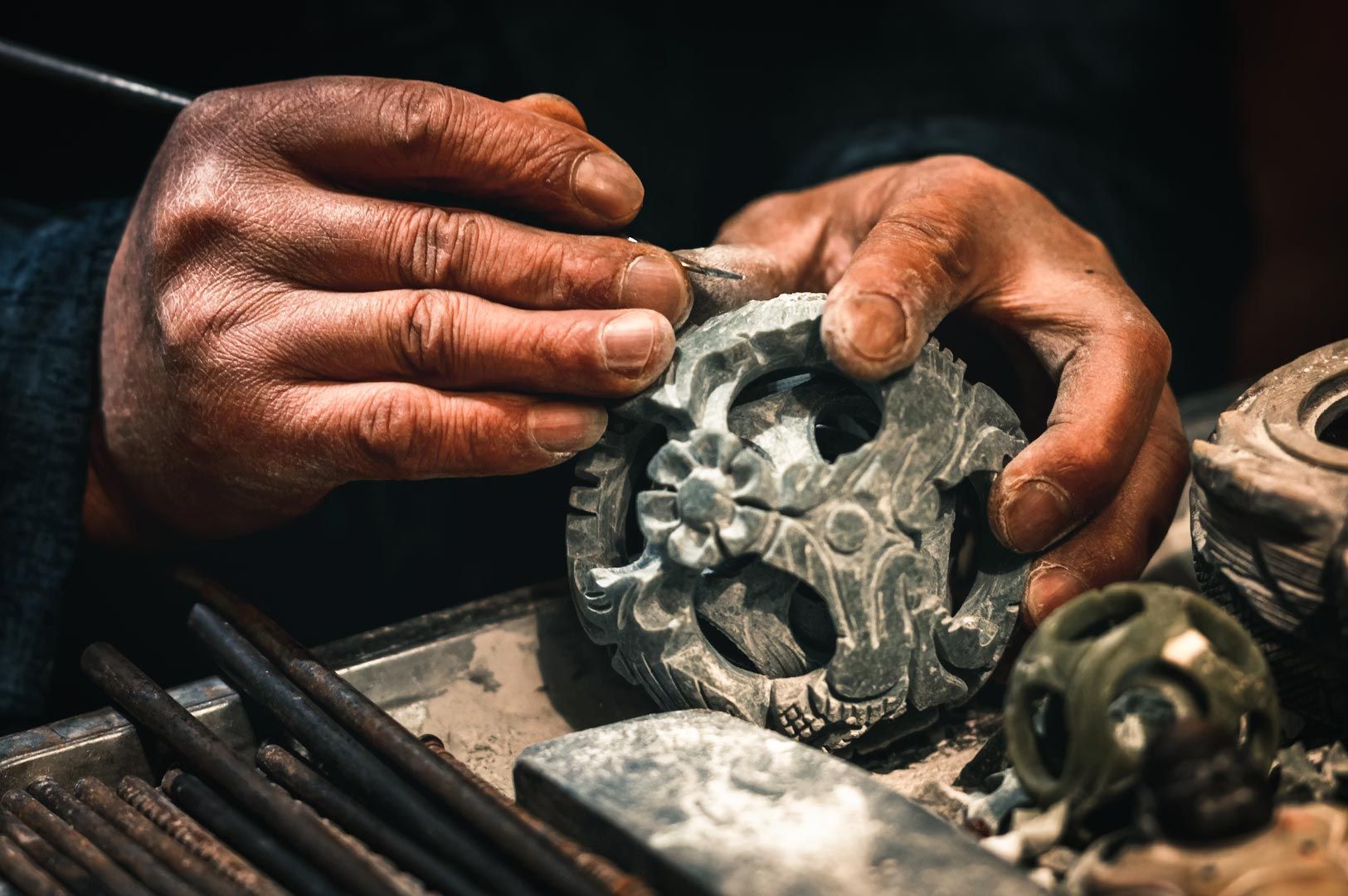 Close-up of a craftsperson carving intricate patterns into a stone ornament using hand tools.