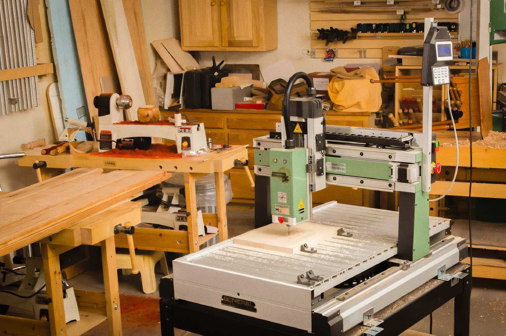 A workshop filled with woodworking tools and equipment, including a CNC milling machine in the foreground and various workbenches and tools in the background.