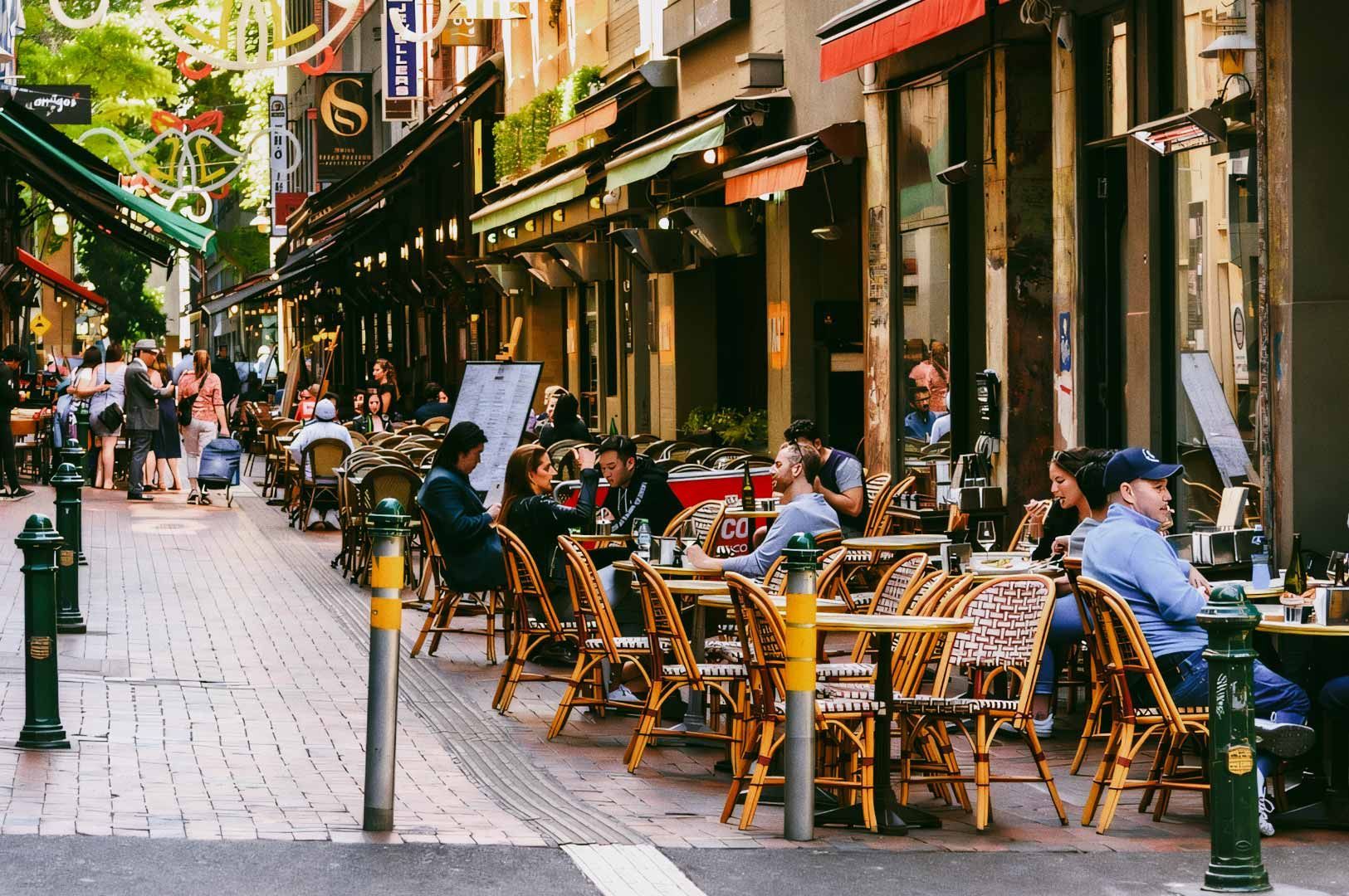 Outdoor café street with people dining at sidewalk tables.