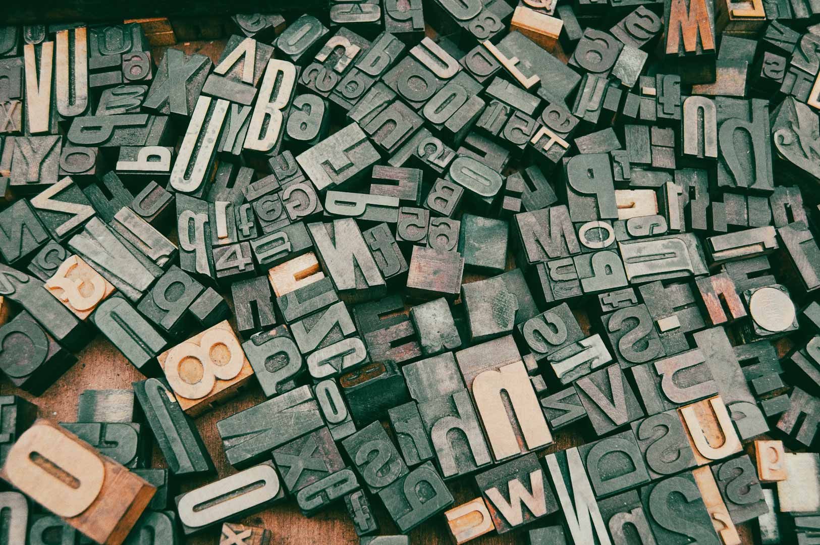 A scattered collection of wooden and metal letterpress type blocks featuring various letters, numbers, and symbols.