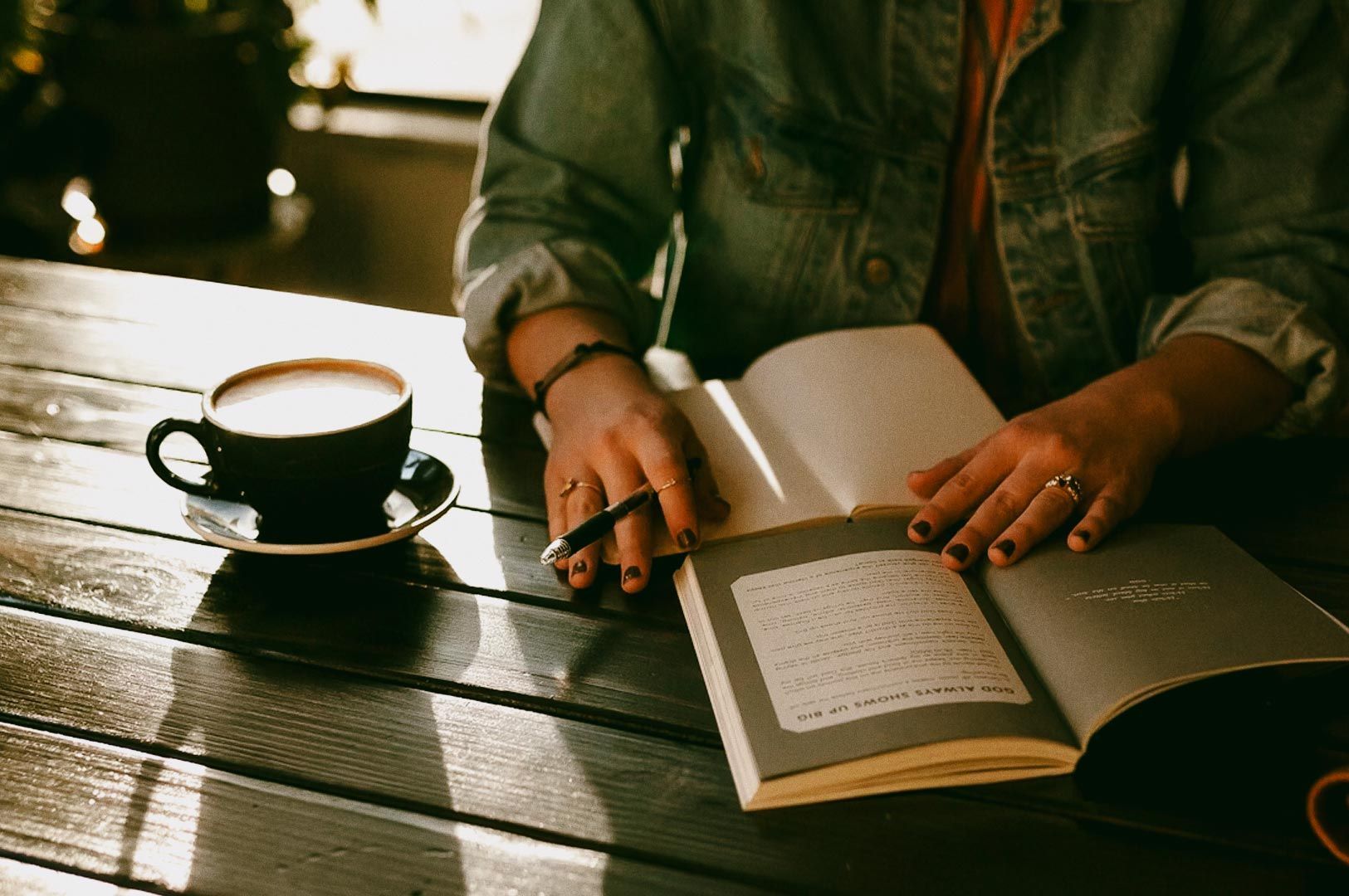 Person reading a book with a cup of coffee on a wooden table.