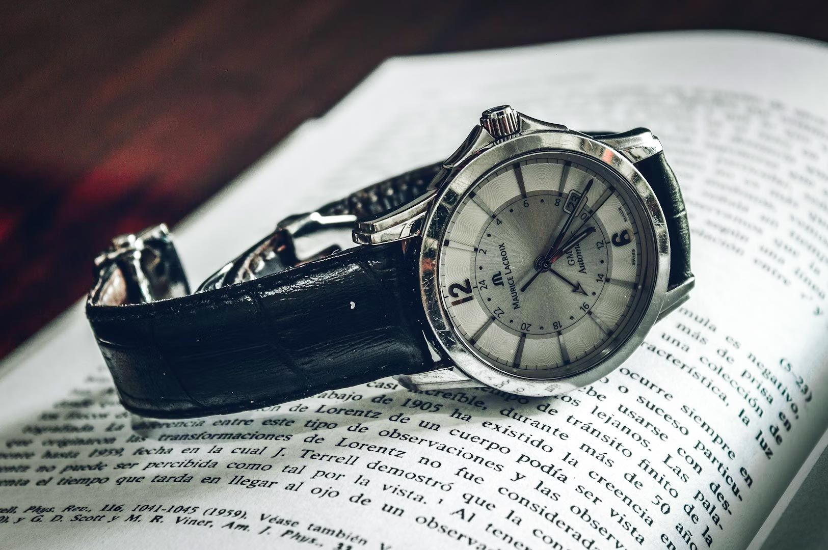 Close‑up of a classic analog wristwatch with a black leather strap resting on the pages of an open book.