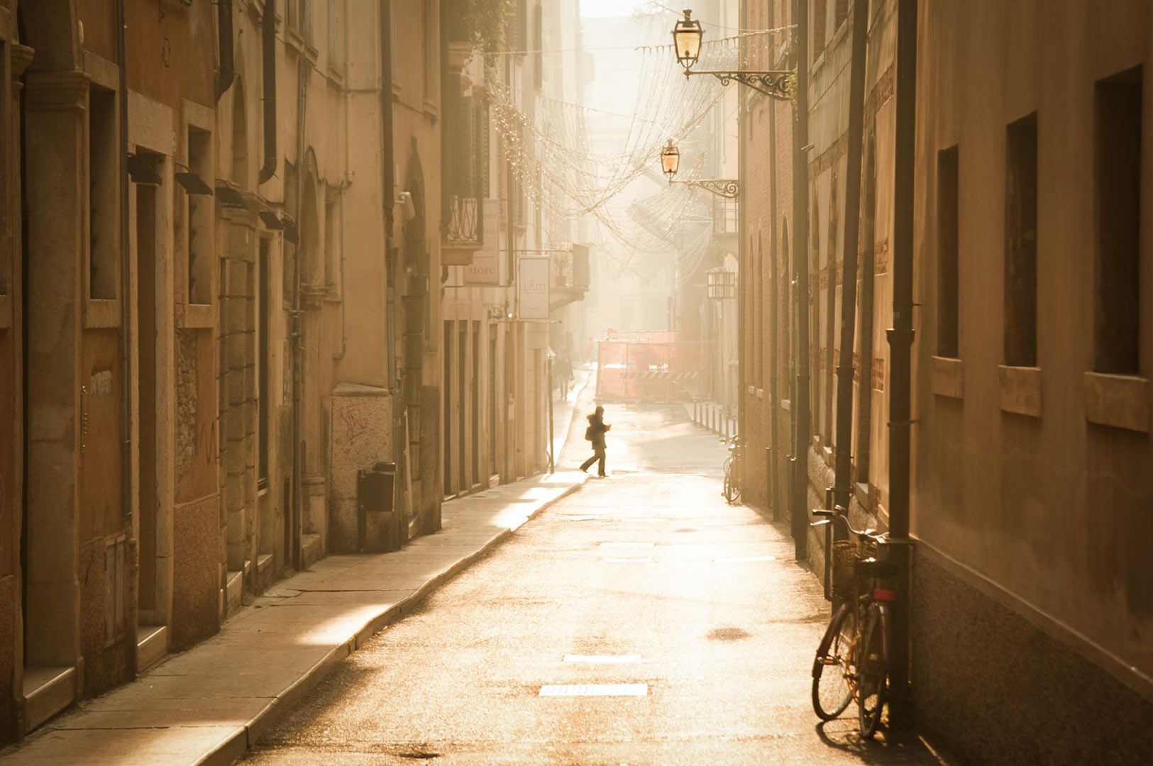 Sunlit narrow street with warm morning light, lined with old buildings and a bicycle parked along the wall.