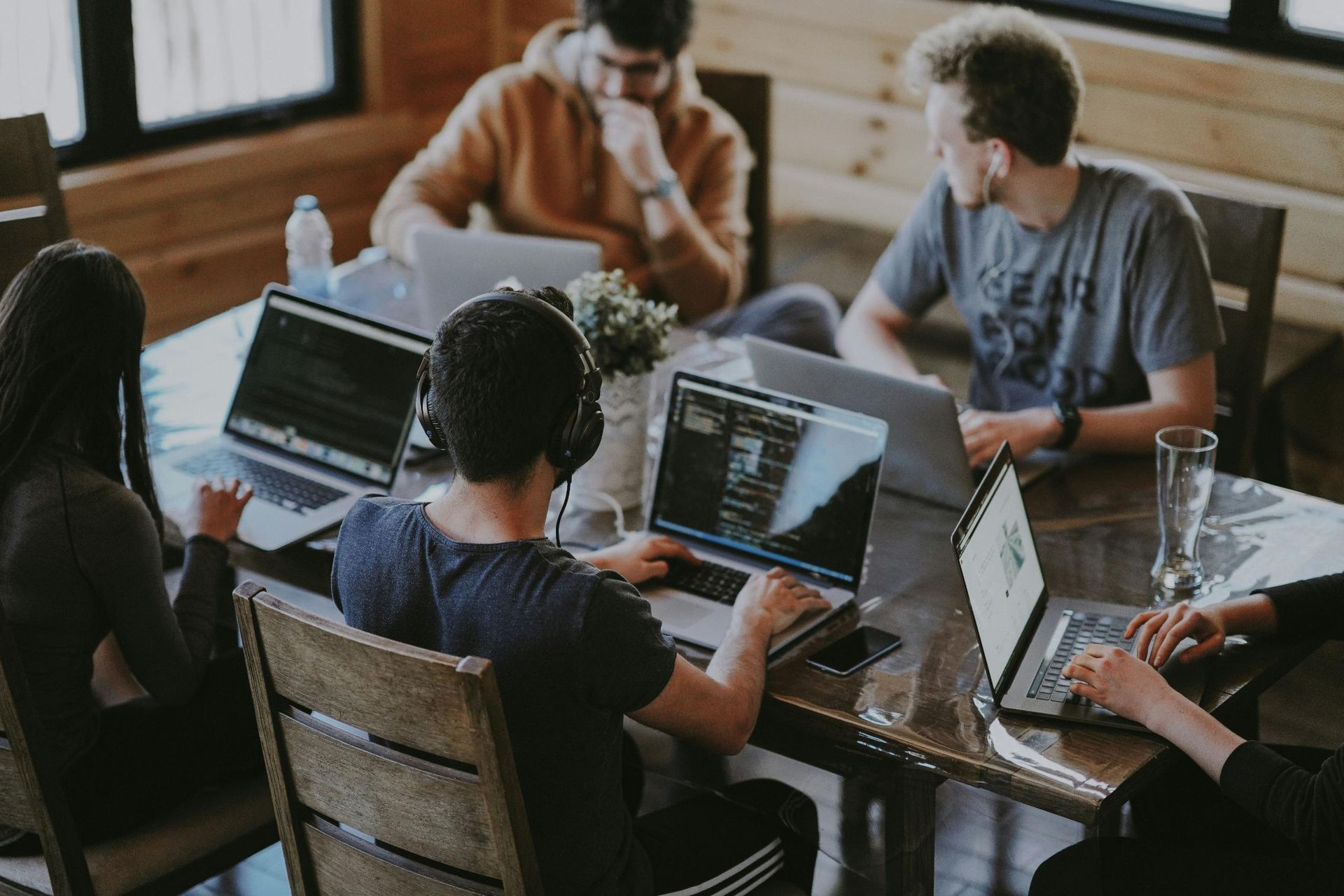 A group of young professionals sits around a wooden table, diligently working on their laptops.