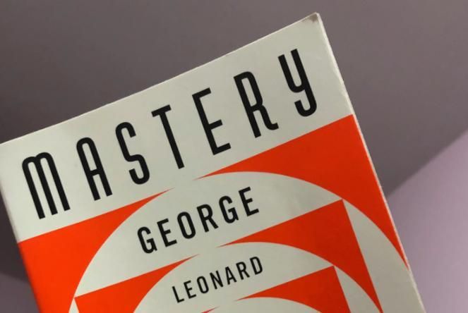 The image features a close-up, angled view of the book cover for Mastery by George Leonard. It showc