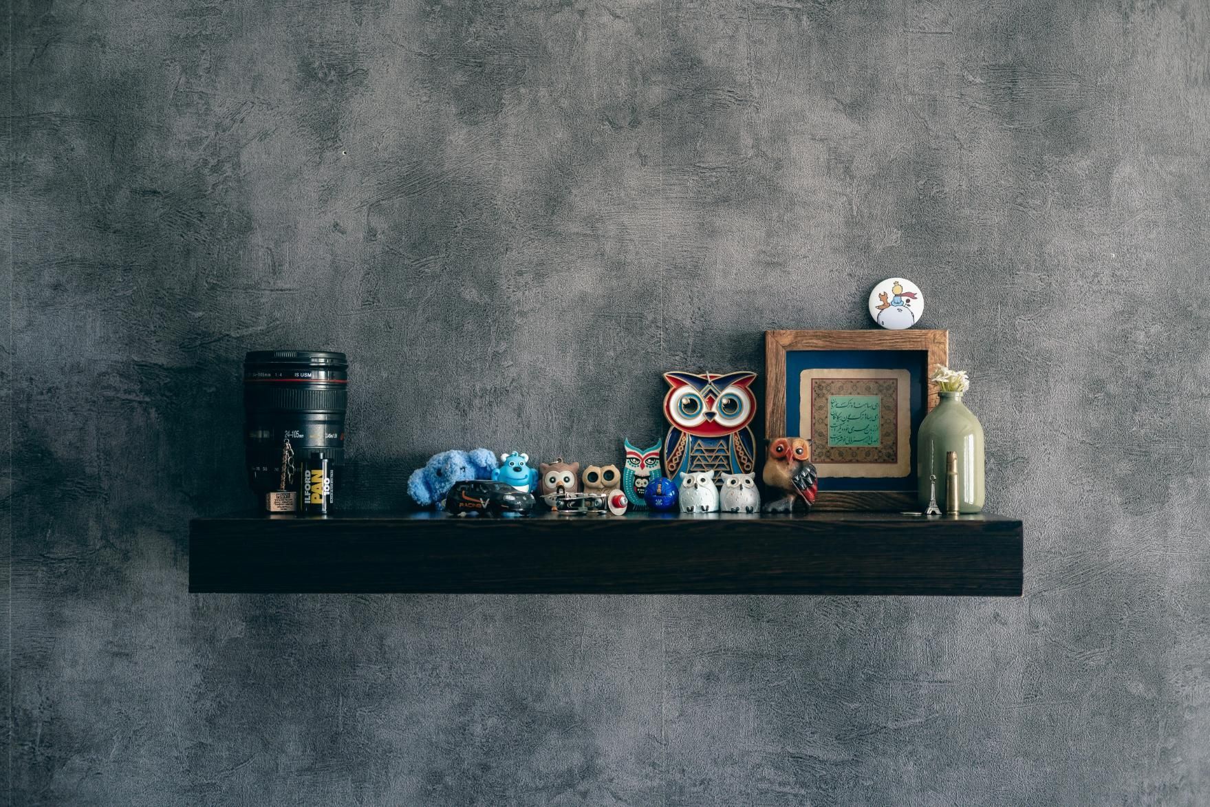A dark wooden floating shelf is mounted against a textured grey wall, displaying an eclectic collect