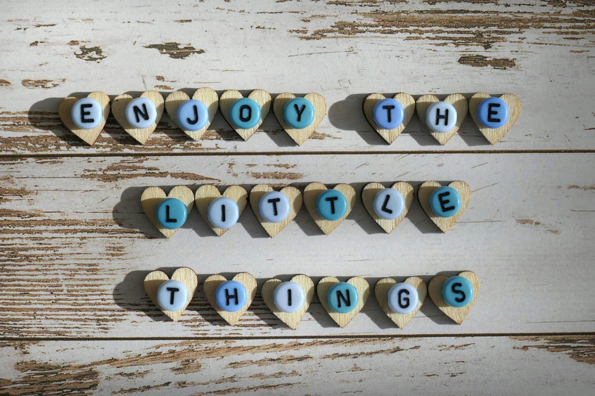 A collection of small, blue circular beads is arranged on top of tiny wooden hearts to spell out the phrase 