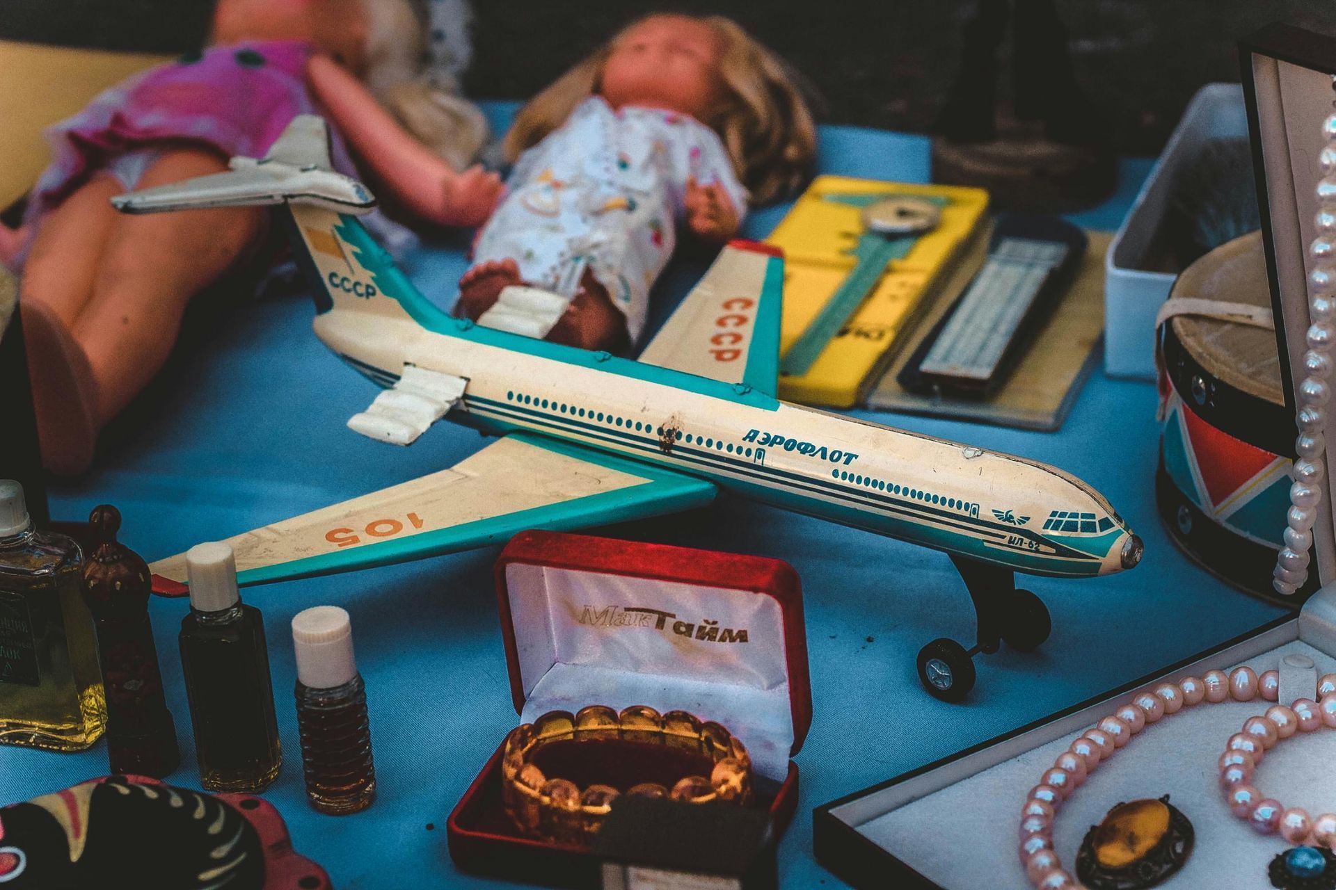 This image captures an assortment of vintage items and toys displayed on a blue surface, centered around a model Aeroflot plane marked with 