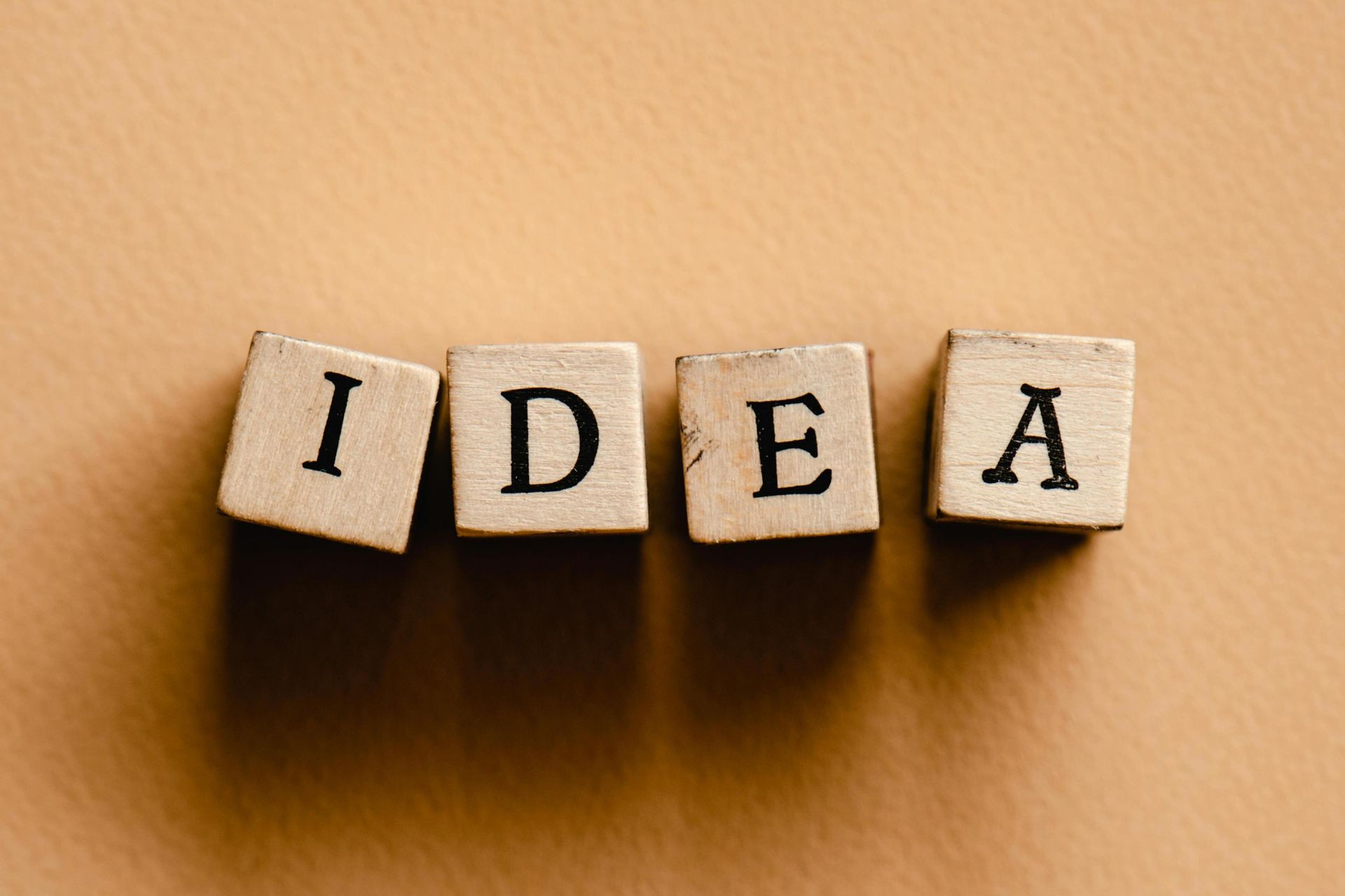 Four small wooden blocks are arranged in a row on a textured, tan-colored surface to spell out the word 