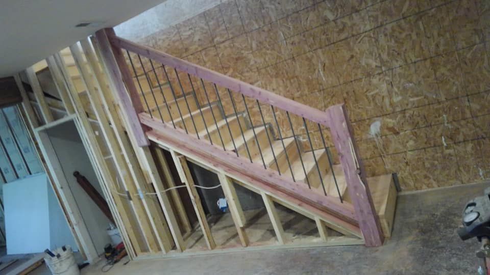A wooden staircase with a metal railing is being built in a room.