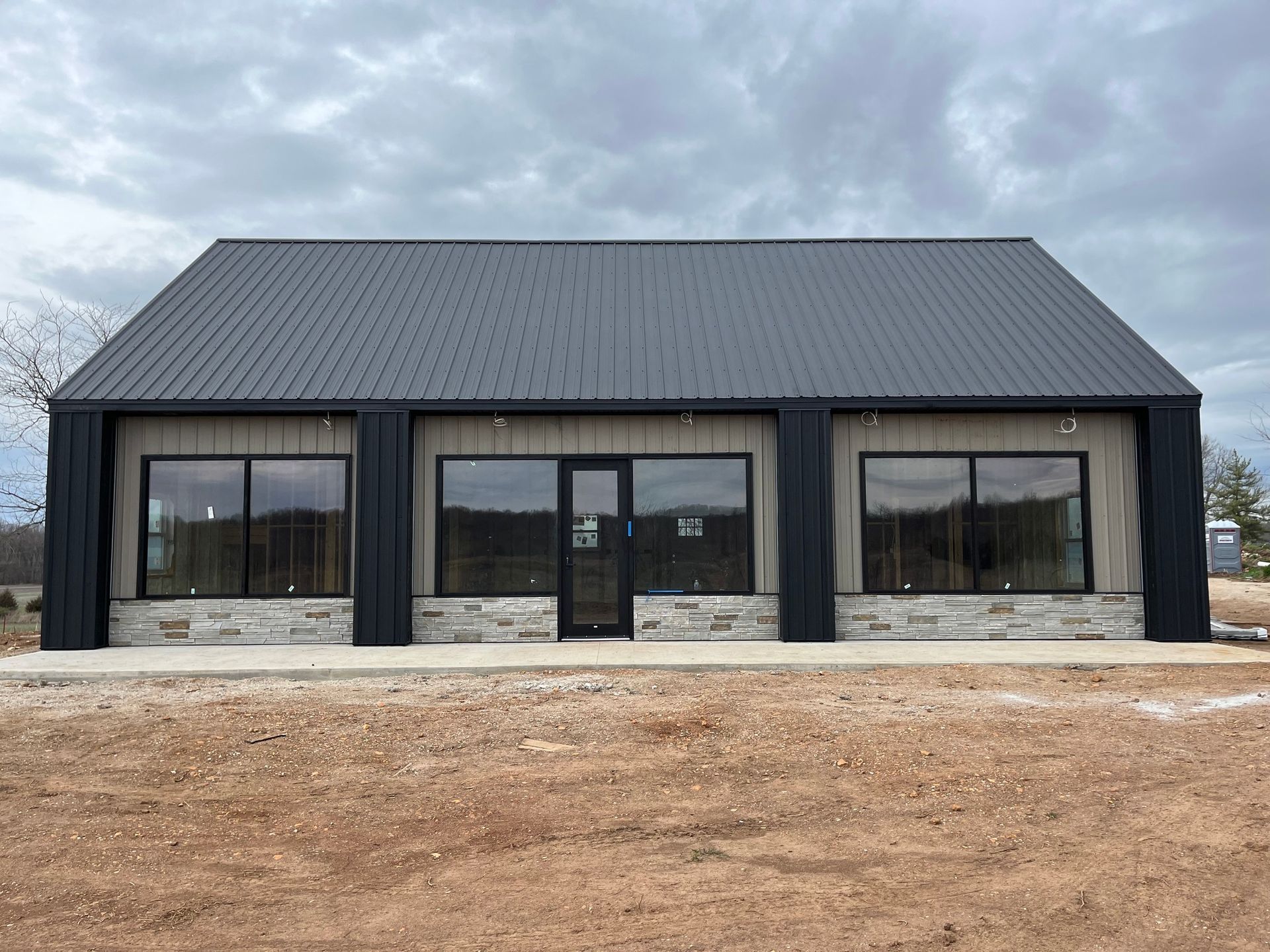 A building with a black roof and a lot of windows is sitting in the middle of a dirt field.