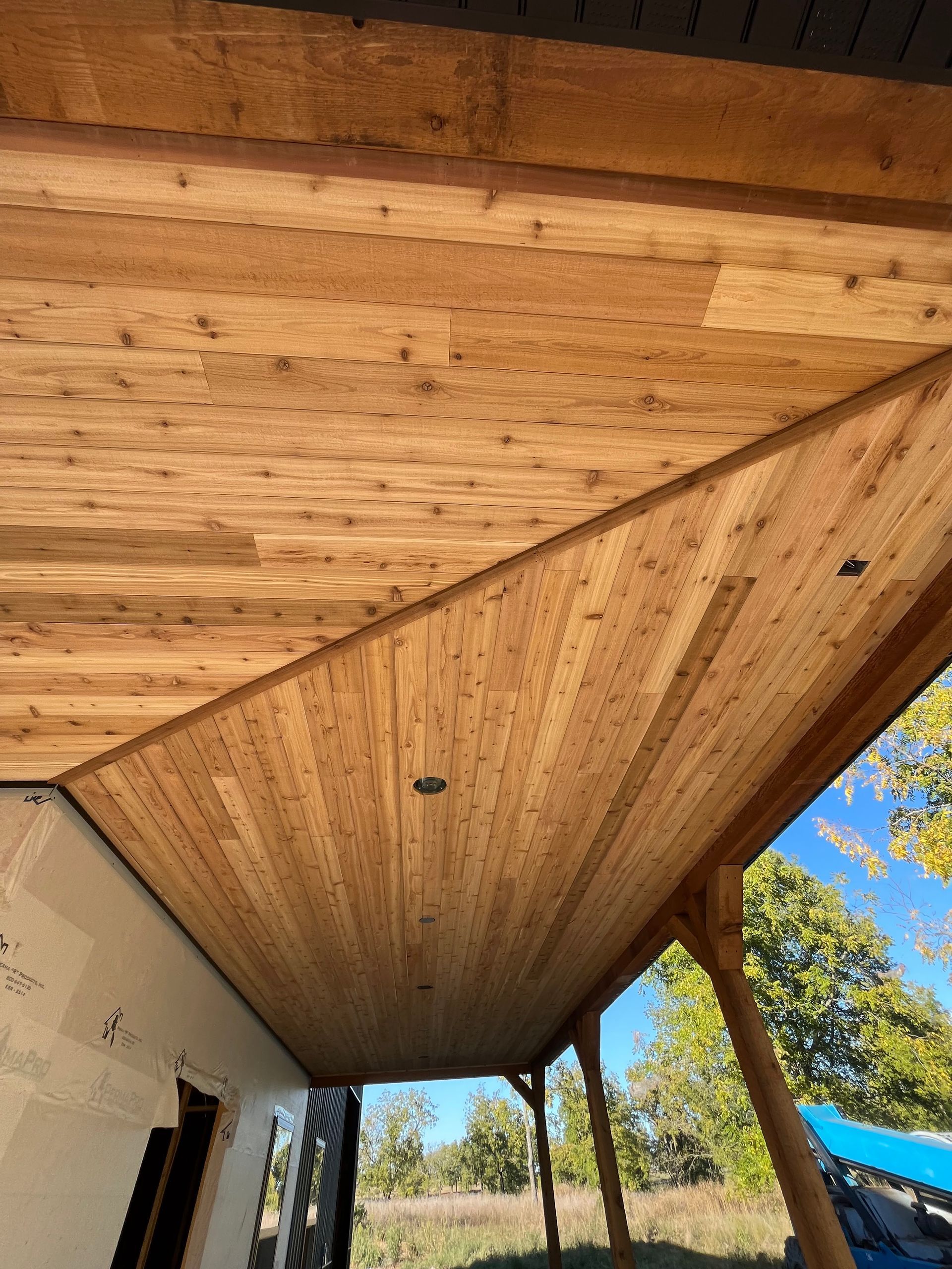 A wooden ceiling on a porch with trees in the background.
