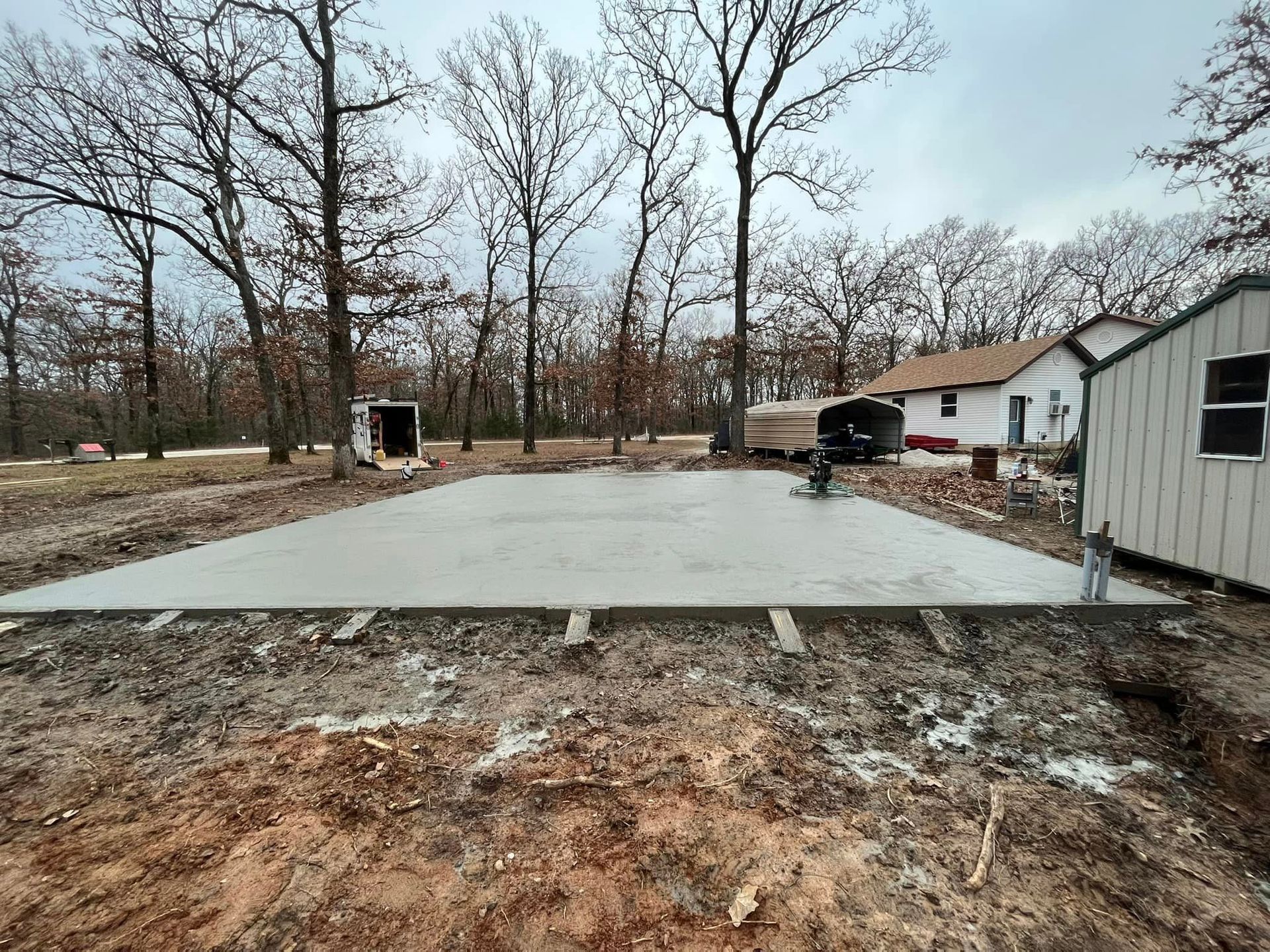 A large concrete slab is sitting in the middle of a dirt field in front of a house.