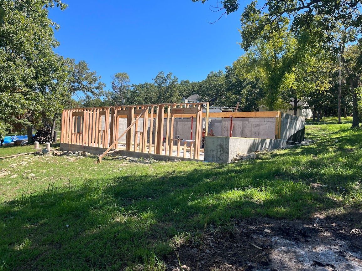A house is being built in a grassy field with trees in the background.