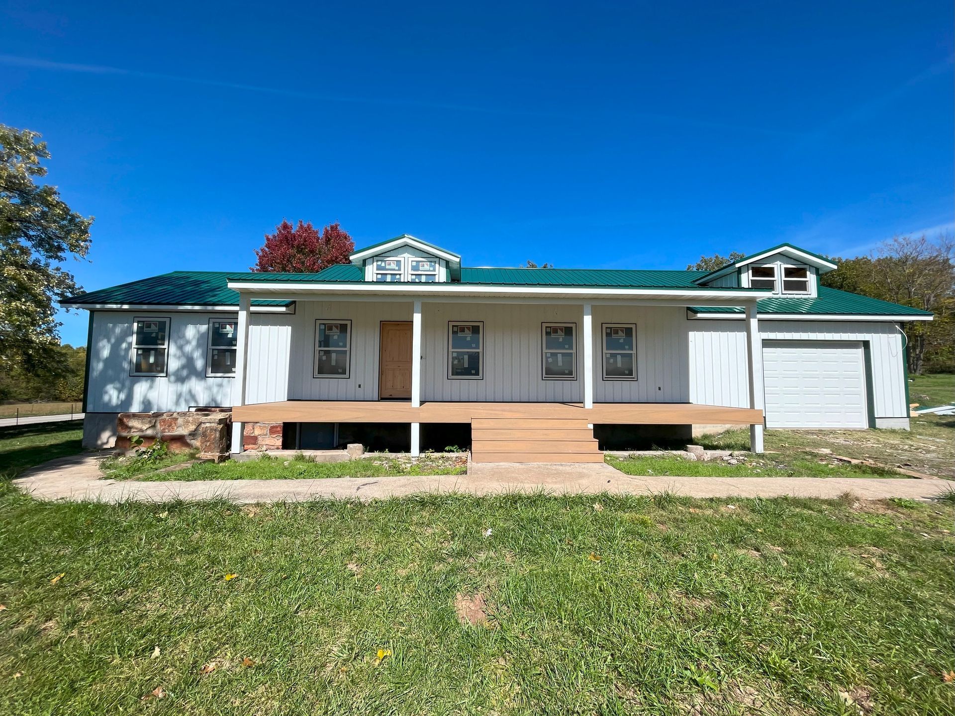 A white house with a green roof is sitting on top of a lush green field.