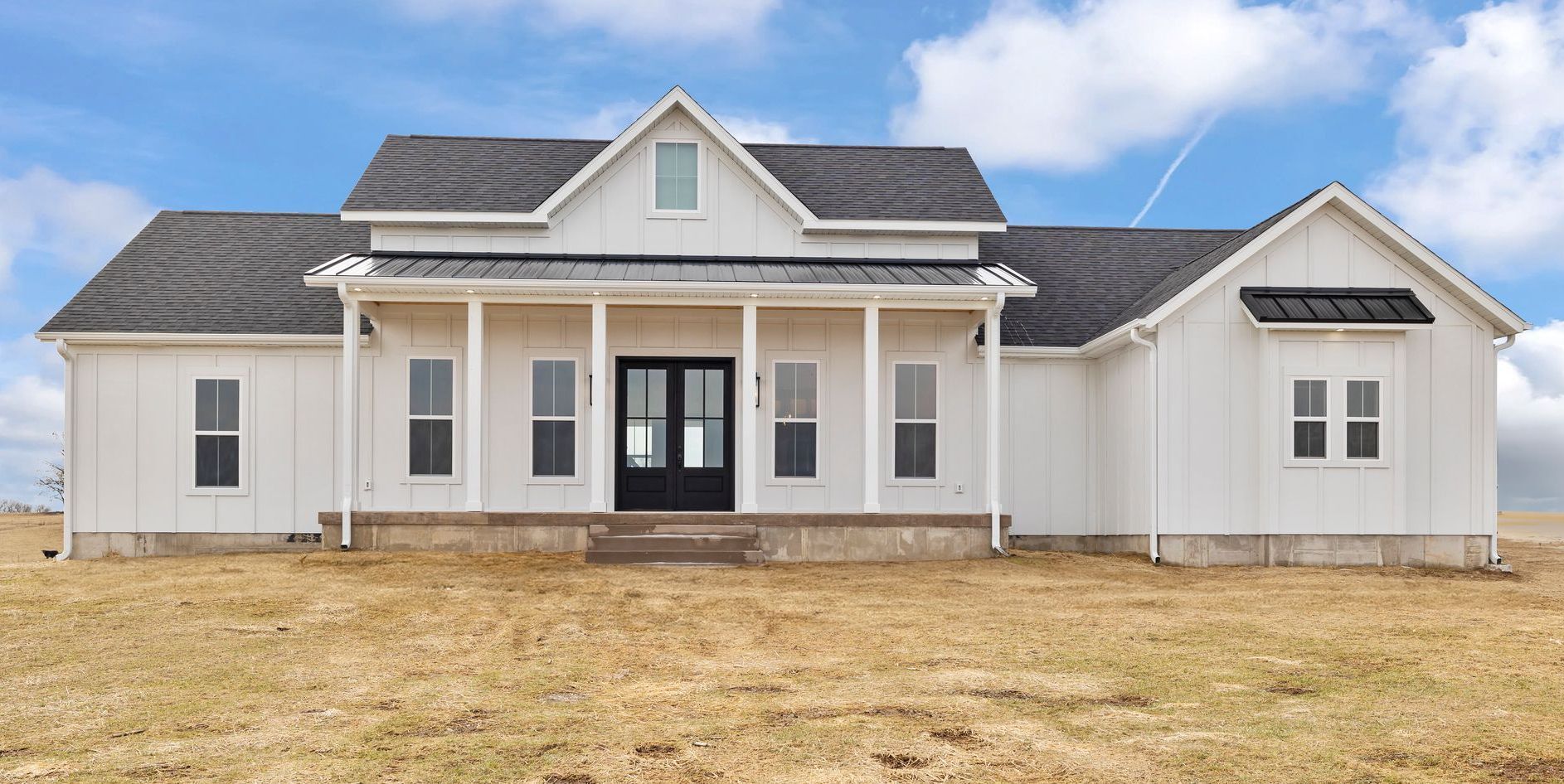 A white house with a black door is sitting in the middle of a field.