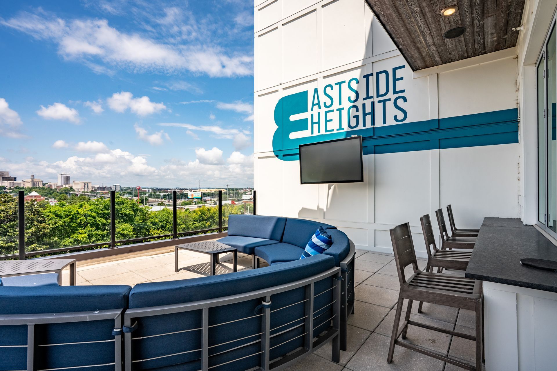 Outdoor patio at Eastside Heights apartments, with blue sectional seating, bar stools, and a cityscape view. 