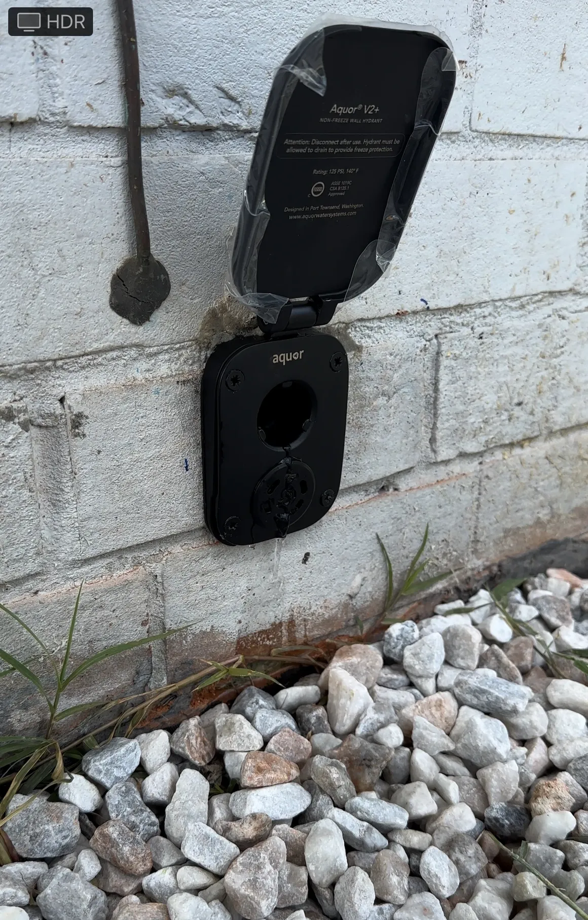 A black electrical outlet is sitting on a brick wall next to a pile of rocks.