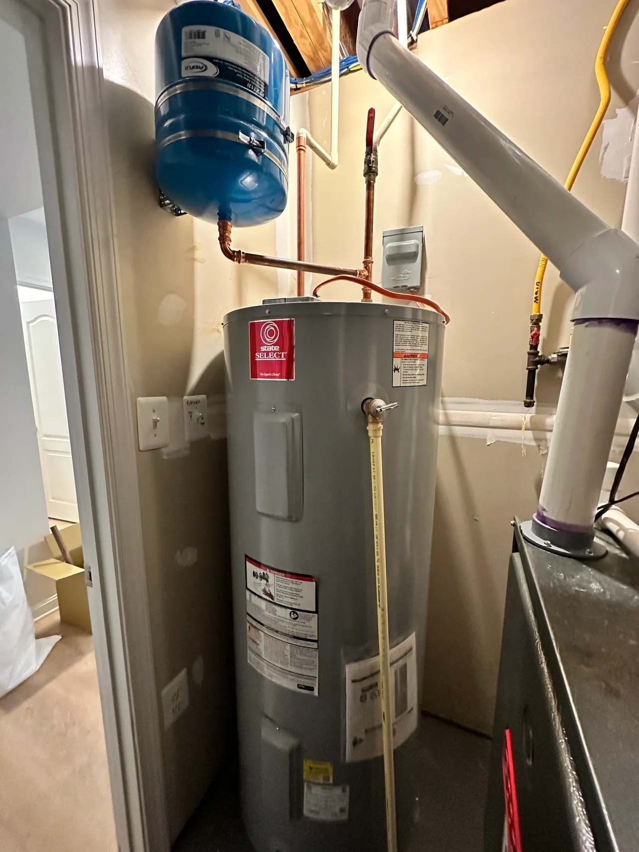 A water heater is sitting in a corner of a room next to a furnace.