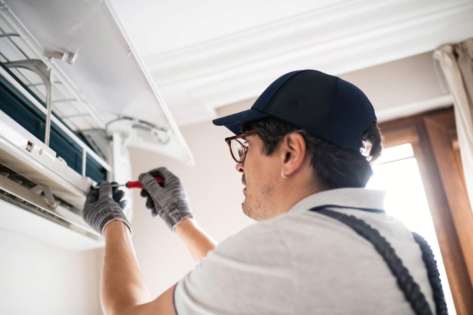 Technician offering air conditioning services by repairing a wall-mounted AC unit at home.