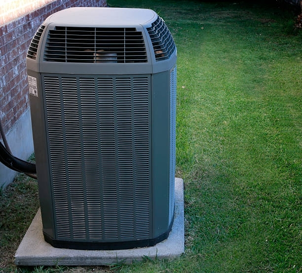 An air conditioner is sitting on top of a concrete base in the grass.