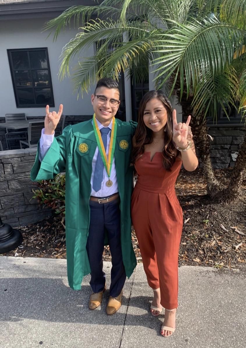 A man in a green cap and gown is standing next to a woman in a red jumpsuit.