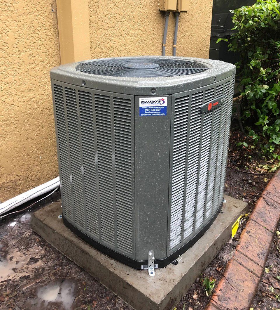 A large air conditioner is sitting on top of a concrete base outside of a building.