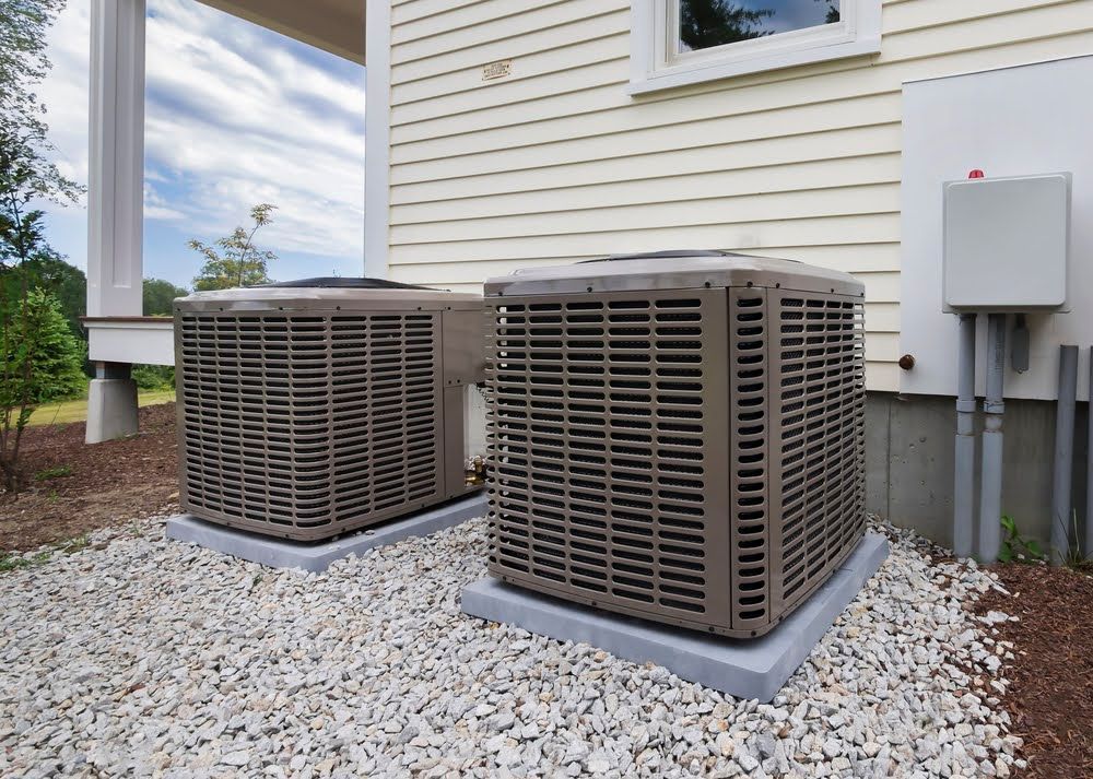 Two air conditioners are sitting on the side of a house.