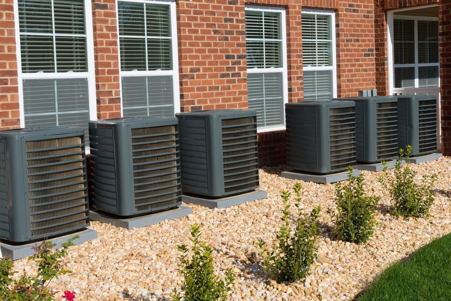 A row of air conditioners are lined up in front of a brick building.