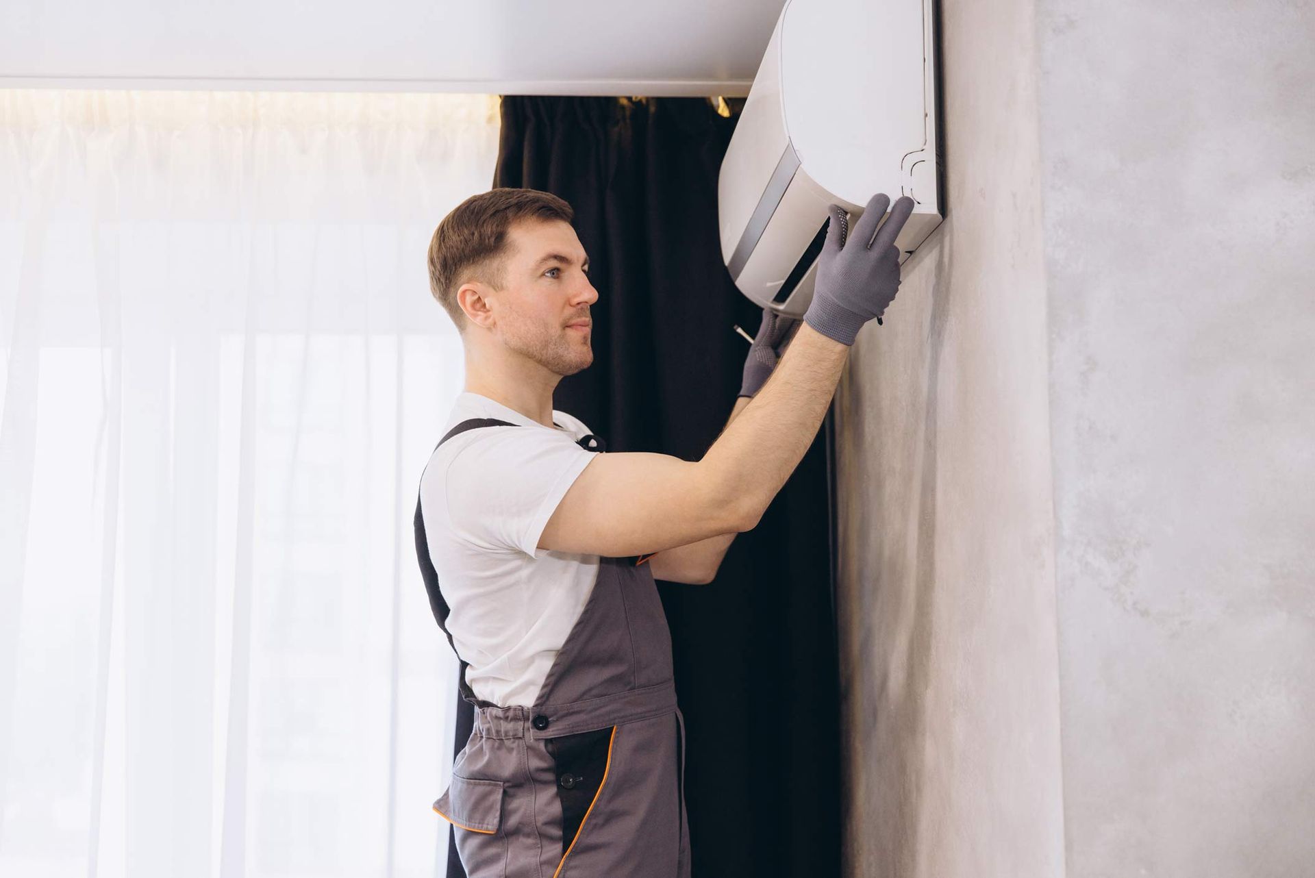 Technician providing air conditioning services while installing a modern indoor AC unit on a wall.
