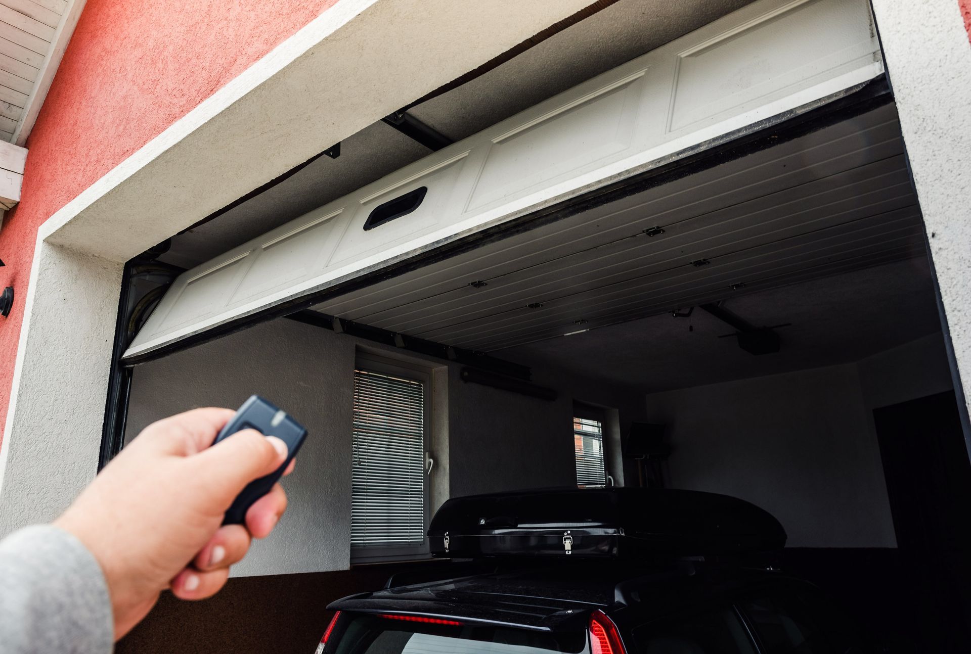 Hand using remote to open garage door with car parked inside.