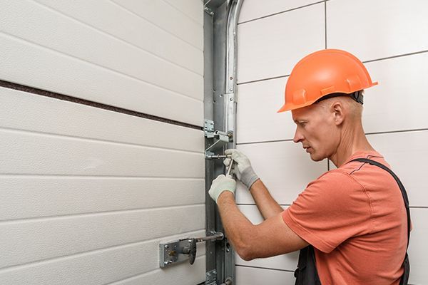 A worker wearing an orange helmet, performing garage door repair and installation. A worker wearing an orange helmet, performing garage door repair and installation.