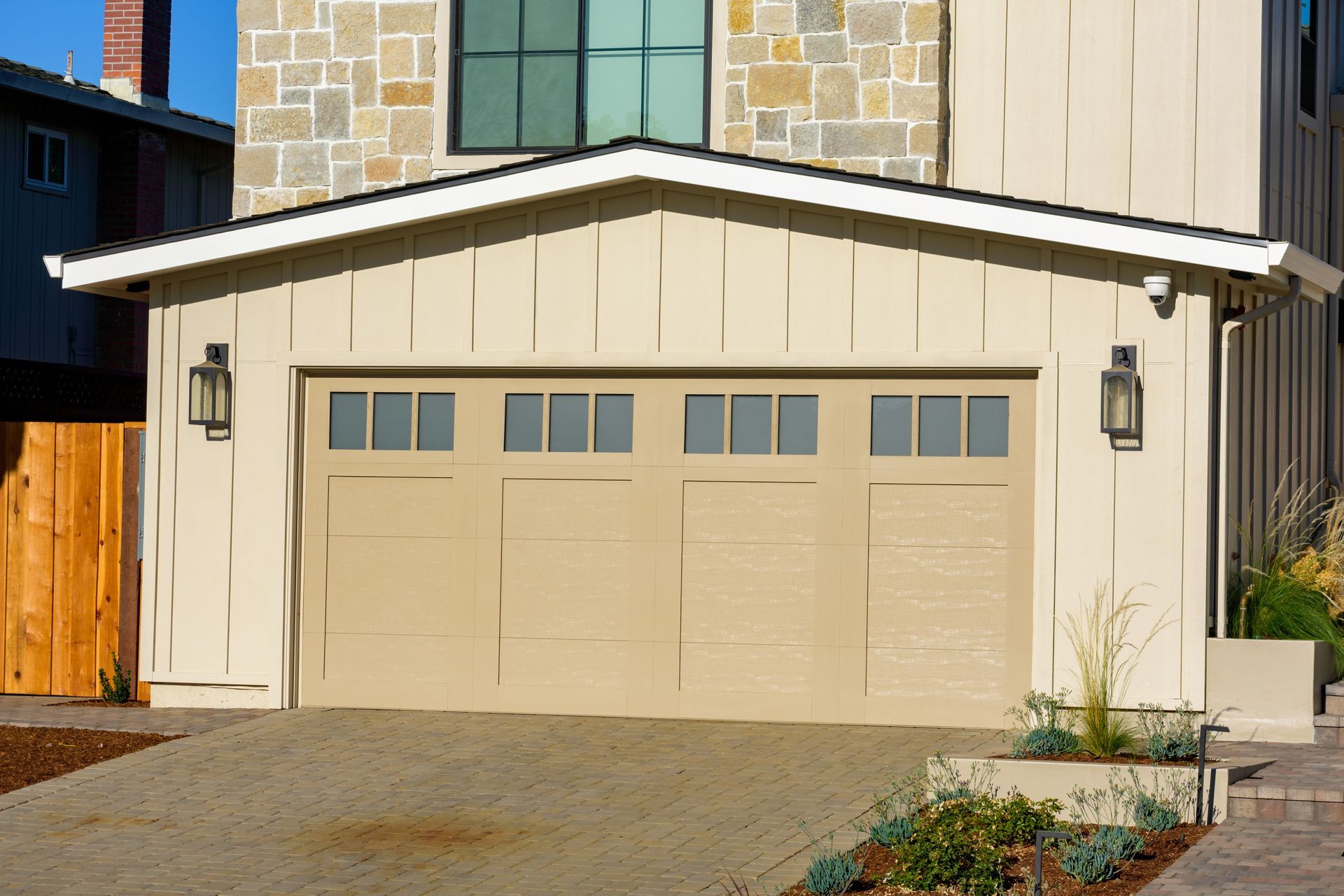A modern beige garage door with four glass panels is part of a contemporary home.