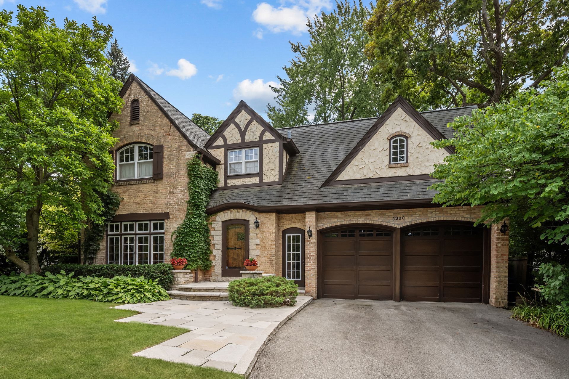 A two-story modern house with beige stucco, a wooden front door, dark gray window frames, and a two-car garage.