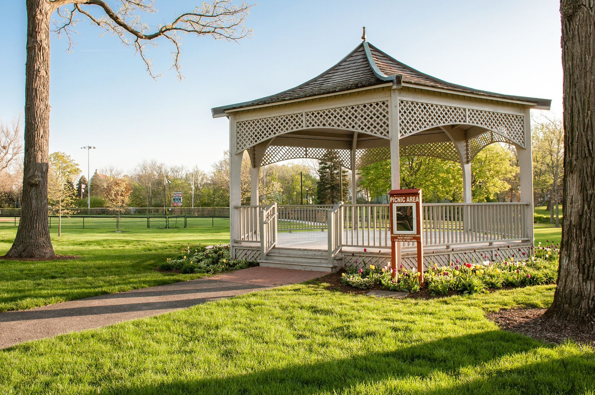 A neighborhood street featuring modern homes with white stucco and wood siding, green lawns, and people walking outside.