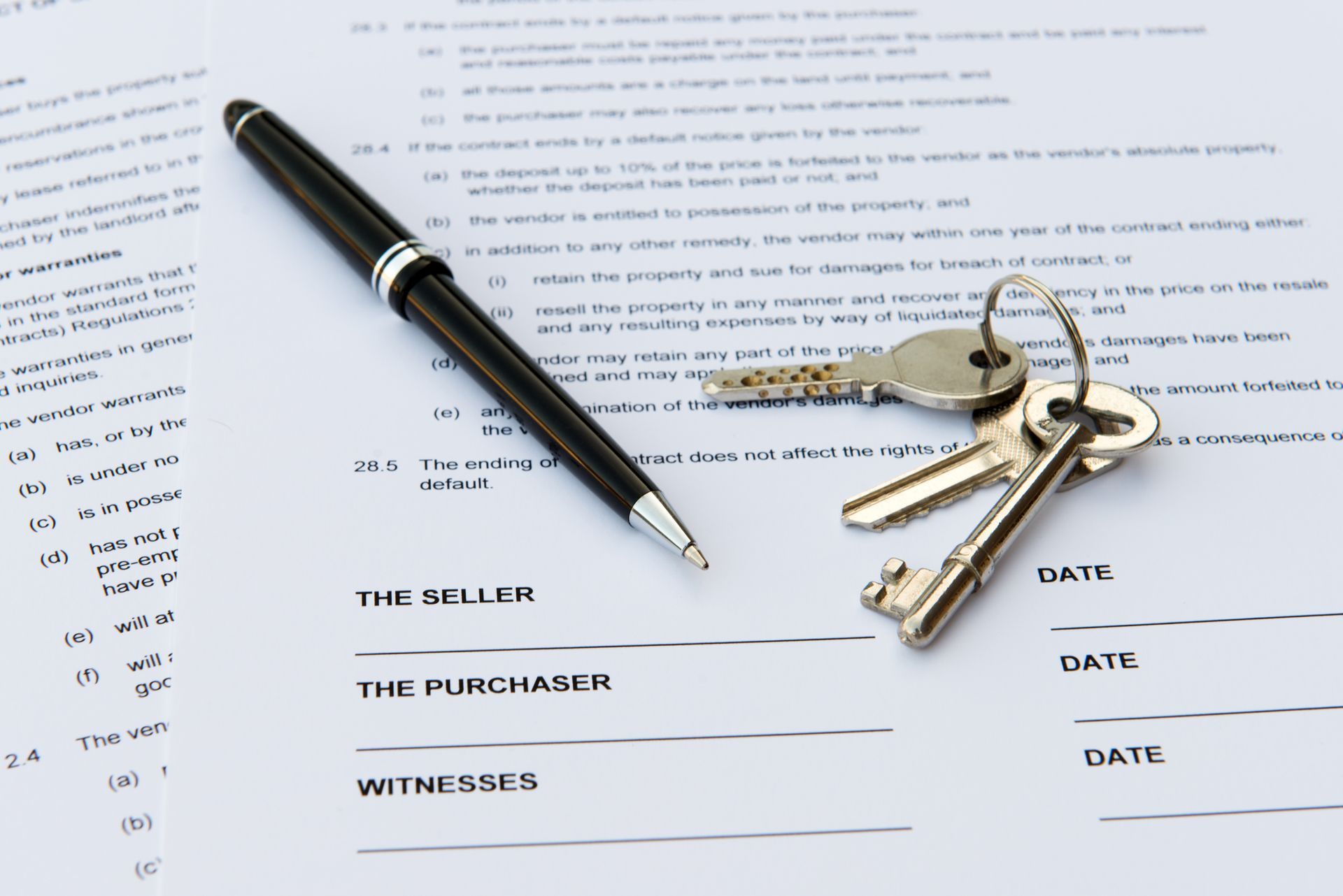 A black pen and a set of silver keys resting on a real estate contract with signature lines for buyer and seller.