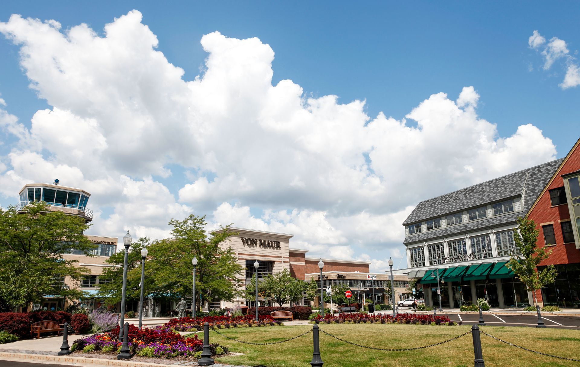 A row of charming, traditional houses with stone facades and grey roofs along a paved suburban street with lush gardens.
