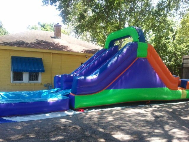 A purple and green bouncy house is in front of a yellow house