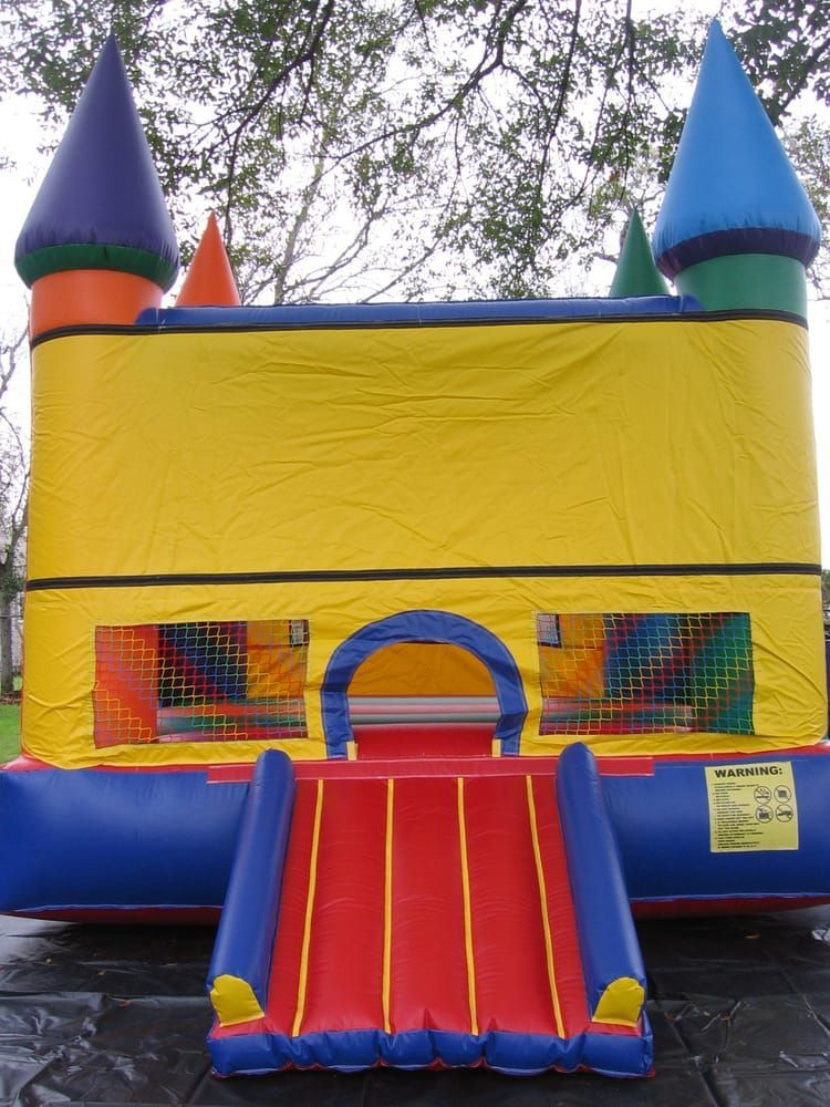 A colorful bouncy house with a slide and trees in the background