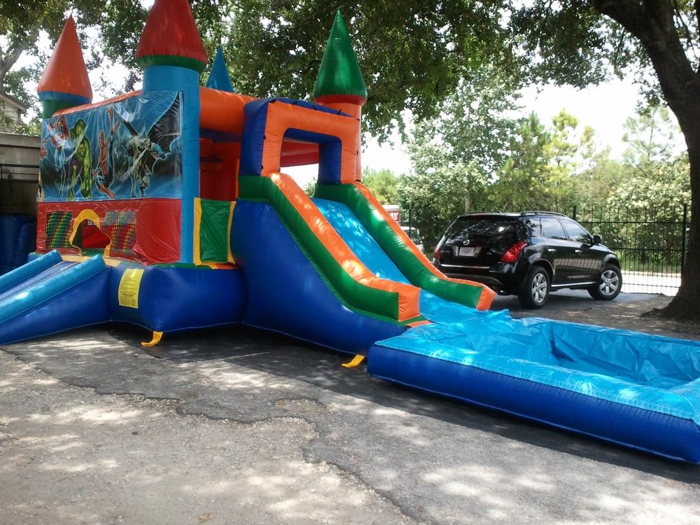 A bouncy castle with a slide and a water slide is parked in a parking lot.