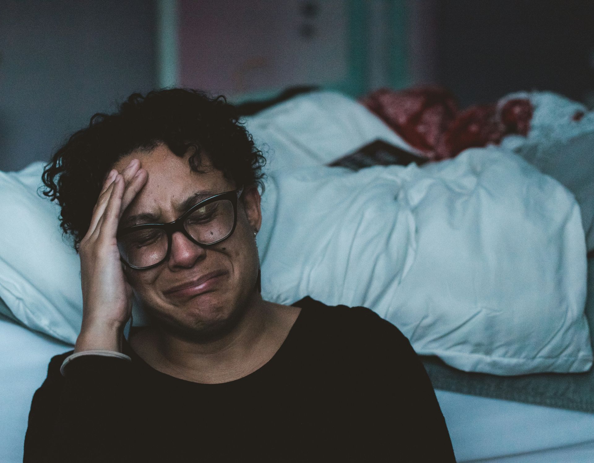 A woman wearing glasses is crying while laying on a bed.