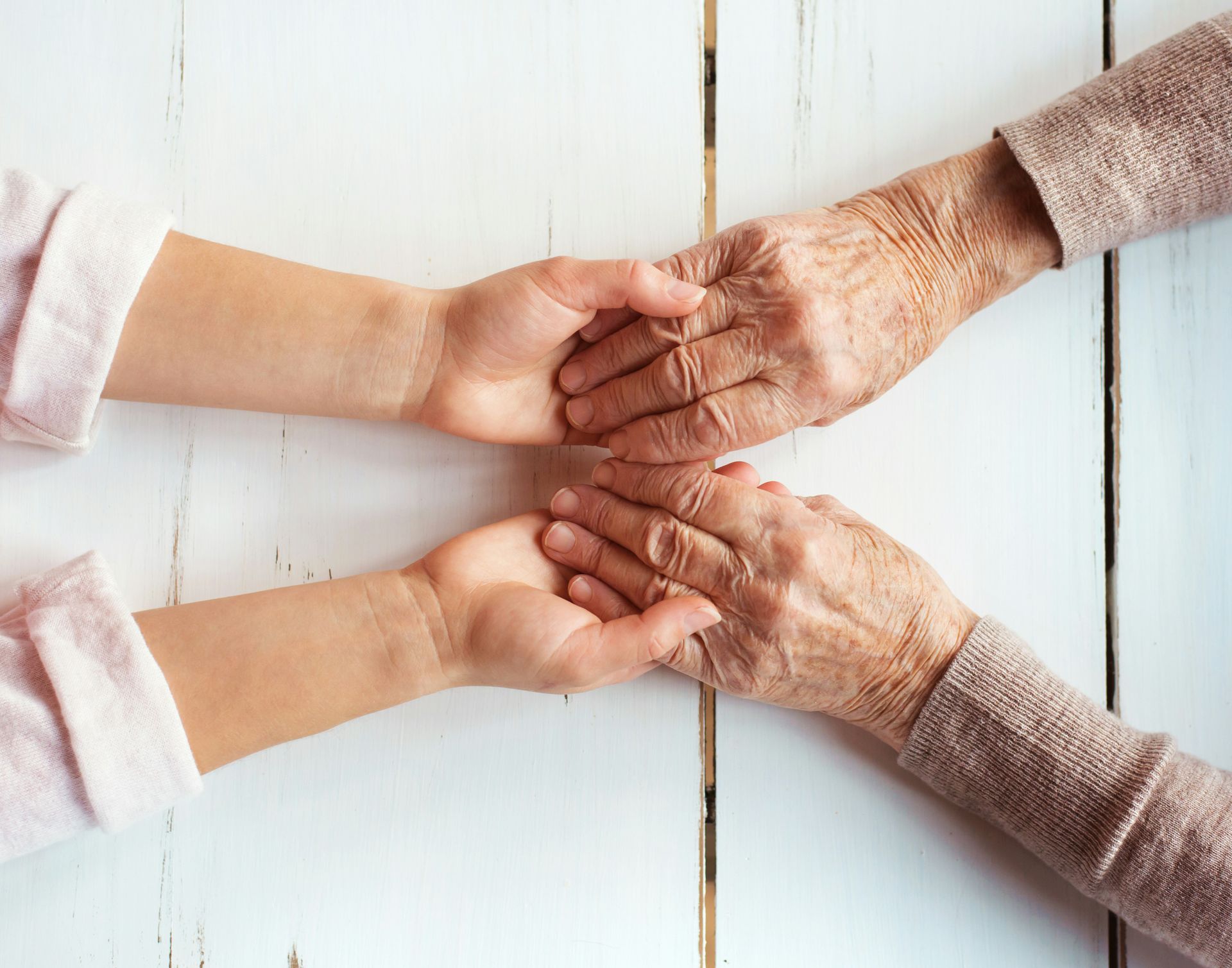 An elderly woman and a young child are holding hands on a wooden table.