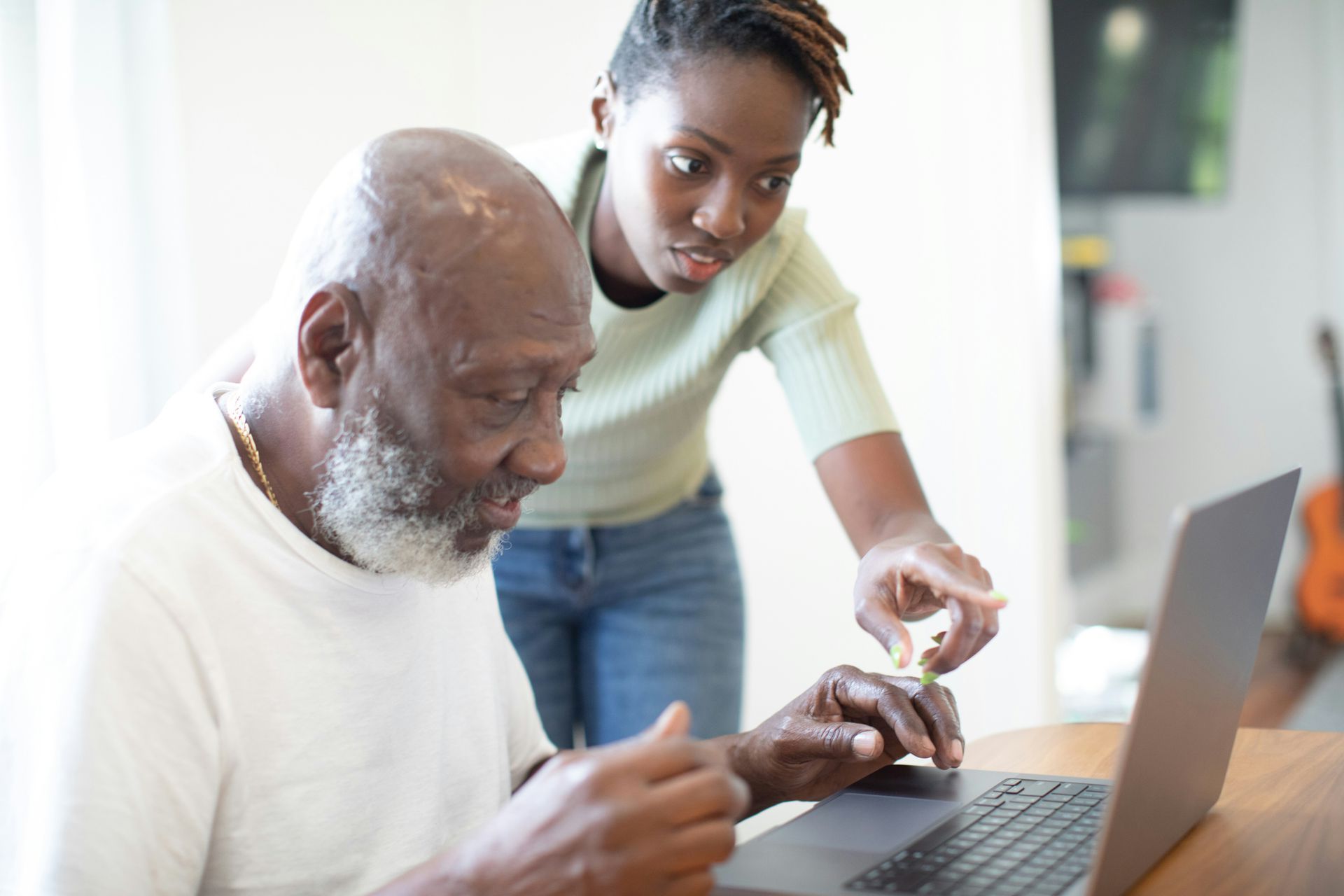 A woman is helping an older man use a laptop computer.