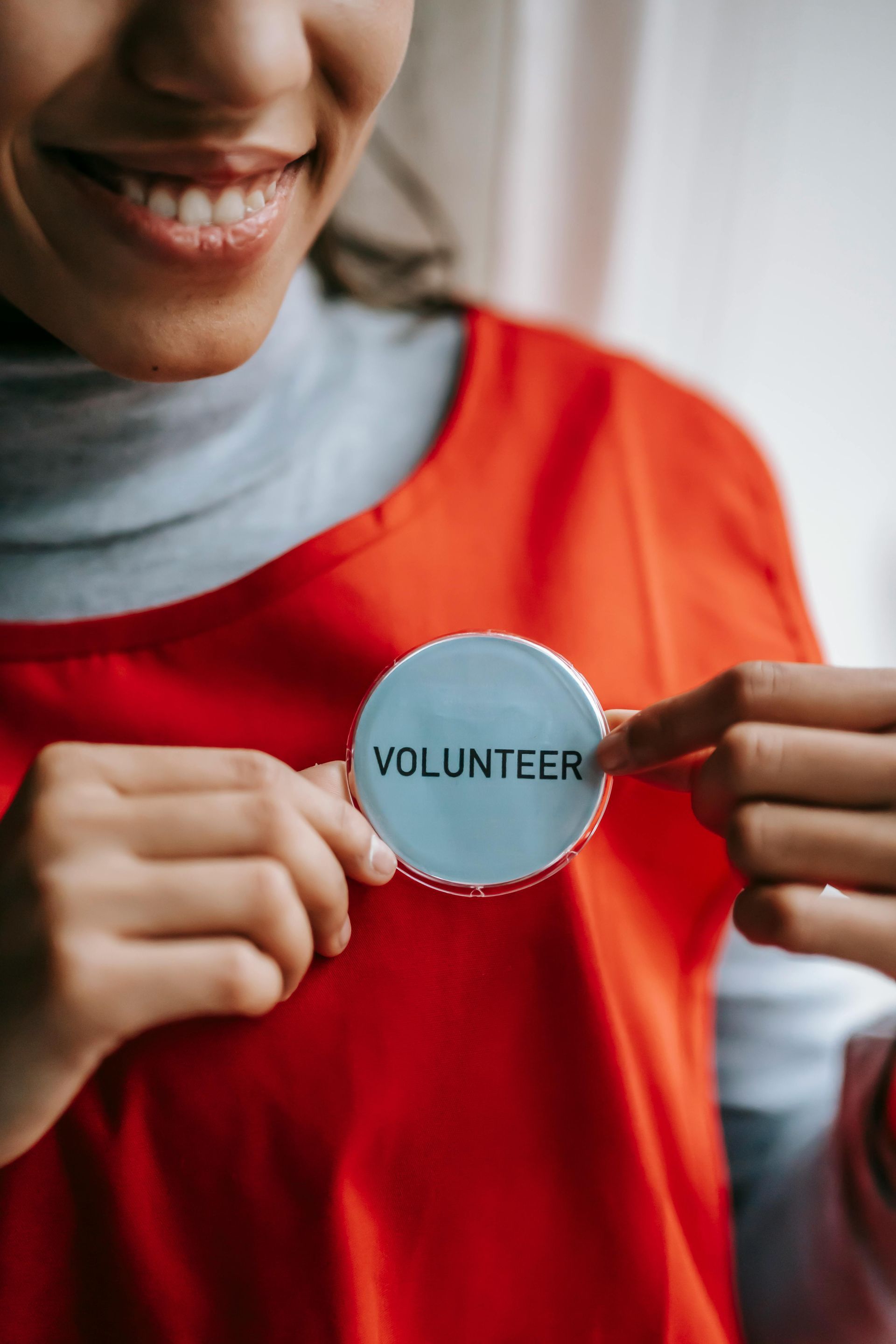A woman in a red shirt is holding a volunteer badge.